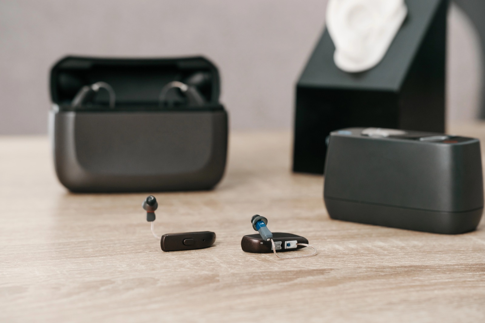 A pair of small modern hearing aids beside their charging case